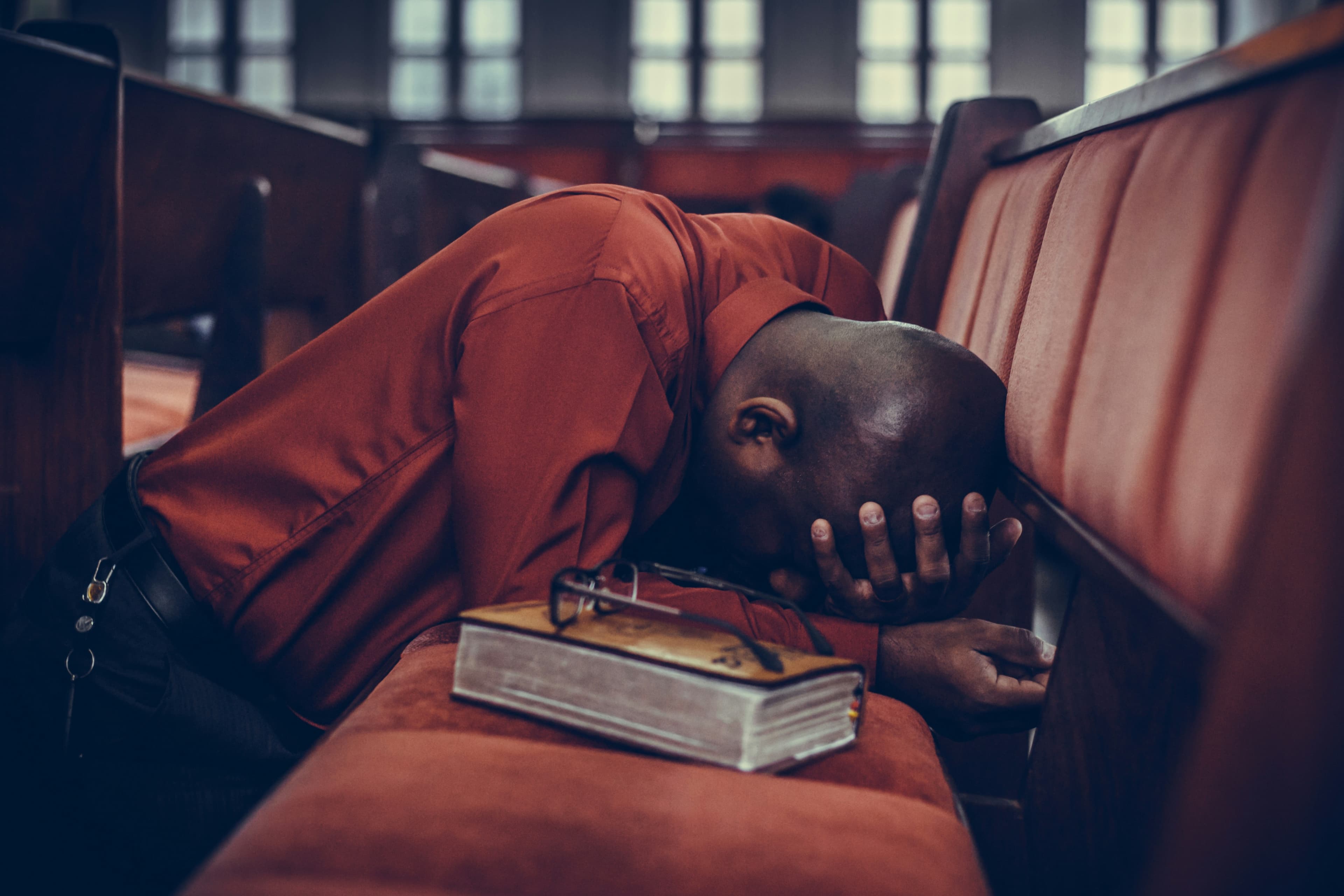 Worshipper praying in a church pew with a Bible nearby.